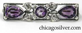 Brooch, silver, rectangular frame with two tear-shaped bezel-set faceted amethyst stones at the ends and a similar round stone at center, with leaves, curling silver stems and silver bead ornament.   Worked frame.