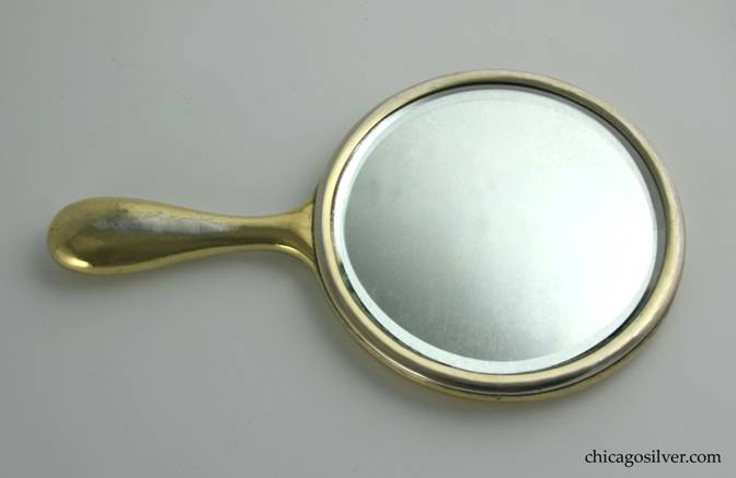 Kalo mirror, hand, with round silvered beveled-glass in round frame above bulbous handle with rounded end.  Covered with gold wash that is worn in places.  Applied McG mono on back.  Heavy and hammered.  9-3/8" L and 5-1/2" W and 5/8" D.  Marked:  STERLING KALO