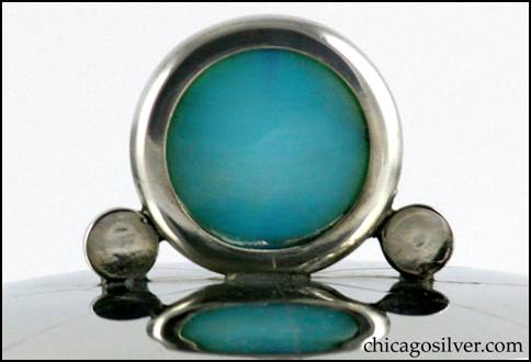 Detail from Rebecca Cauman box, round, pewter, straight-sided on flat bottom with four small ball feet, and removable tightly fitted slightly domed lid.  Lid has large upright round translucent blue stone finial in round see-through frame with a small solid round disk on either side, and eight chased lines radiating outward from the center.  