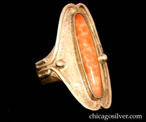 Forest Craft Guild ring, silver, with large oval face, notched at top and bottom, and with small silver beaded decoration at the sides, centering a large thin oval bezel-set mottled orange cabochon Victoria stone.  Applied wire along the edge of the face curves around in two small oval loops at both sides.