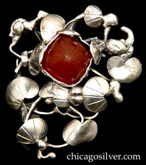 Mary Gage pin, composed of freeform open wirework frame holding arrangement of chased and hammered lily pads and silver beads, surrounding a square carved square cabochon bezel-set carnelian stone