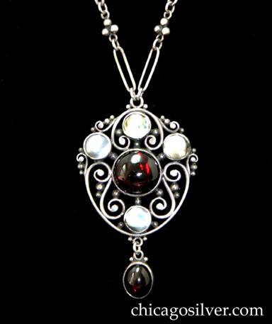 Frank Gardner Hale pendant on chain, stylized shield form frame with handwrought sterling scrolls and beads with a round, central garnet cabochon with three bezel-set blister pearls above and one below finished with a garnet drop.  Original paper clip chain with oval links alternating with 3 bead clusters, toggle clasp.