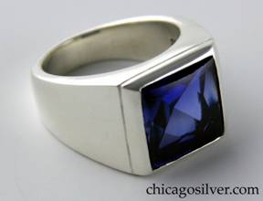 Kalo ring, silver, thick and heavy, square front centering faceted blue stone with chased line around edge, round wide shank, small square cutout behind stone.