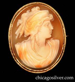 Lebolt brooch, carved bezel-set shell cameo of woman in classical clothing looking to the right, with tan background, inside oval gold frame with applied ropelike decoration around outside