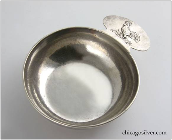 Kalo porringer, round, flat bottom form with tab handle and applied wire rim.  Handle has chased and repouss decoration of rooster standing on grass.  