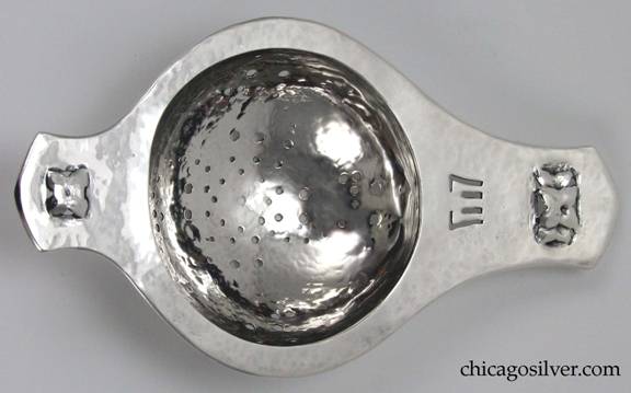 Rokesley tea strainer with short slightly pointed tab handle at one end, and longer one at the other.  Round bowl with spiral pierced design of large and small holes.  Pierced and repoussé floral designs at each end, and small pierced geometric fork-like design at on the larger tab handle.  Heavily hammered surfaces.