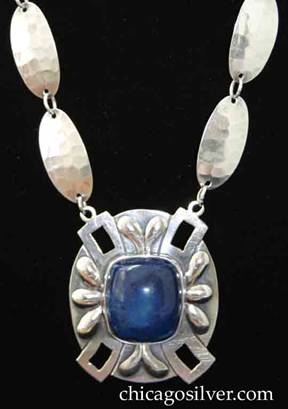 Art Silver Shop necklace, composed of 16 hammered oval links connected by small loops, centering a large oval lapis pendant.  Pendant has four rectangular cutouts at the "corners" on a broad flat rim, alternating with two applied teardrop shaped decorations at top and bottom, and three on each side.  At the center is a large deep square bezel-set cabochon lapis stone with rounded corners.