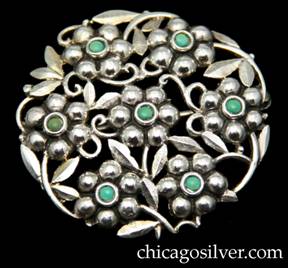 Brooch / pin, silver, with turquoise stones, European 935 silver.  Round frame with six repoussé blossoms arranged in a circle with a seventh one at center, each blossom centering a small round bezel-set cabochon turquoise stone.  Blossoms are connected by silver leaves and curving stems.